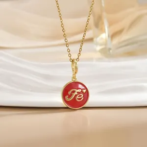 Close-up of gold chain necklace with red enamel FE letter charm and heart detail