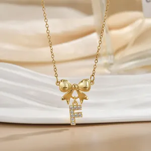 Detailed view of golden bow necklace with letter F pendant inlaid with zircon crystals