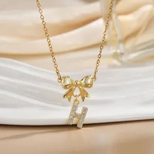 Close-up of golden bow necklace featuring a sparkling zircon-encrusted letter H pendant