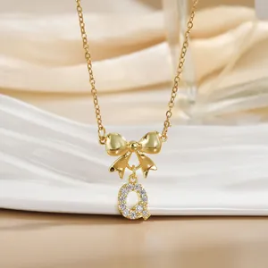 Macro shot of gold bow and crystal-encrusted letter Q pendant on sleek ceramic