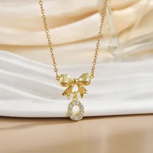 Detail of gold bow necklace with letter O pendant inlaid with zircon on ceramic tray
