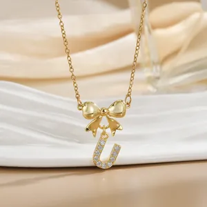 Close-up of golden bow necklace with crystal-paved letter U pendant on silk background