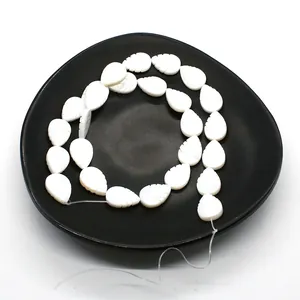 Macro detail of white leaf-shaped shell beads with fine carved texture on a dark tray