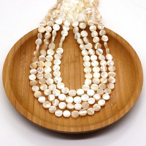 Flat round natural white mother of pearl shell beads in a wooden tray for jewelry making