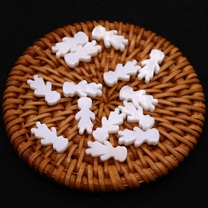 Natural white shell girl and boy shaped loose beads on a brown rattan mat with black background