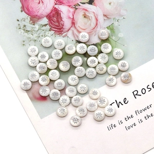 Detailed view of round white shell beads with silver sunburst star patterns for jewelry DIY