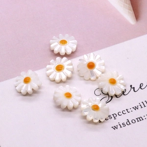 Macro view of white daisy seashell charms with yellow centers for DIY jewelry making