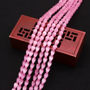 Macro shot of faceted pink cat eye stone teardrop beads arranged on a red wooden box