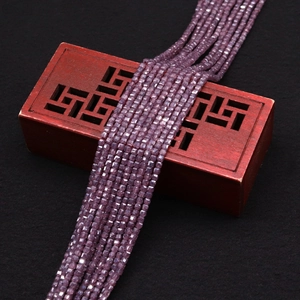 Macro shot of deep purple faceted sugar cube zircon beads draped over a vintage wooden box
