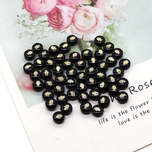 Macro shot of circular black freshwater shell beads with gold Hamsa Hand patterns for DIY jewelry