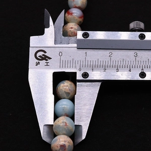Close-up of caliper measuring the diameter of natural stone beads with blue and rust texture