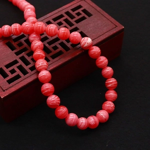 Red marble-patterned round synthetic beads on a decorative vintage wooden display box