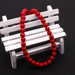 Collar de perlas de vidrio rojo pulido presentado sobre un banco blanco en miniatura