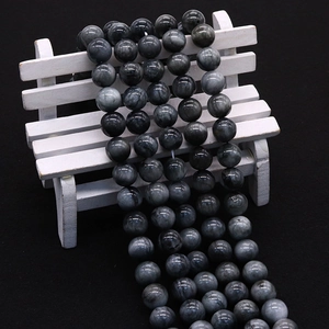 Natural gray eagle eye gemstone beads with chatoyancy on a decorative wooden bench