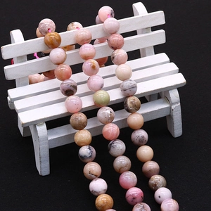 Natural pink opal round beads for jewelry making displayed on a small white wooden bench