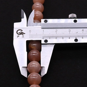 Macro shot of an 8mm orange moonstone bead being measured with a metal caliper tool