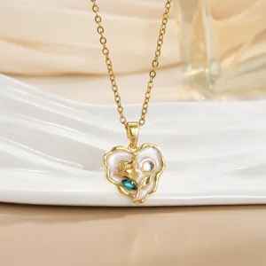 Macro detail of 18k gold heart pendant with a white enamel finish and green rhinestone