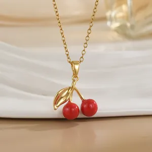 Gros plan d'un collier pendentif cerise avec émail rouge et chaîne dorée sur fond clair
