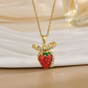 Elegant gold titanium strawberry necklace with sparkling bow detail on white wavy pedestal