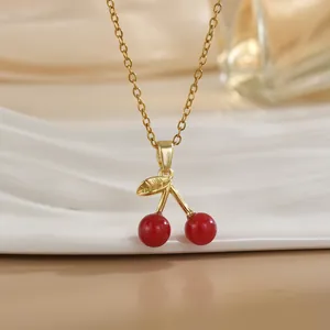 Détail d'un collier pendentif cerise rouge avec feuille dorée sur plateau céramique