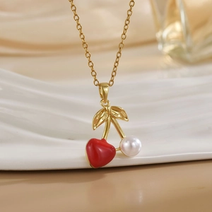 Close-up of gold cherry pendant necklace featuring a red heart and a white pearl charm