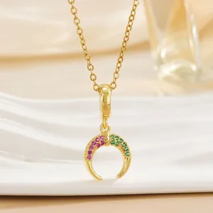 Detail shot of a gold crescent pendant with purple and green crystals on a link chain