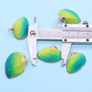 Vue macro de pendentifs coquillages jaune-vert mesurés avec un pied à coulisse doré