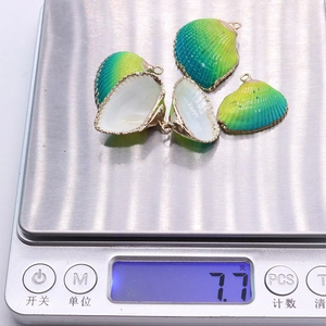 Vue détaillée de quatre pendentifs coquillages verts sur une balance pesant 7,7g