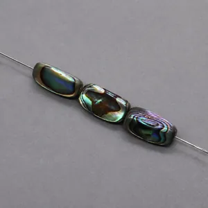 Dettaglio macro di tre perle rettangolari in conchiglia di abalone con riflessi iridescenti