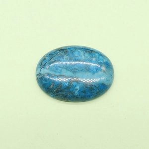 Polished oval blue tiger eye stone cabochon with natural marble texture on green surface