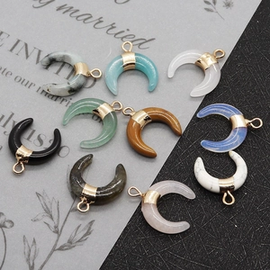 Ten crescent moon pendants in assorted natural stones with gold bails on a dark textured surface