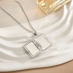 Silver book-shaped locket necklace with rainbow zircon inlay on white ceramic tray