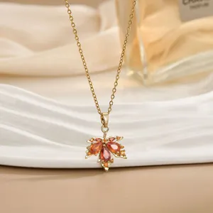 Dettaglio di una collana con ciondolo a foglia d'acero dorata e gemme arancioni su seta