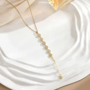 Macro detail of golden Y-shaped tassel necklace with micro-pave zircons on ceramic tray