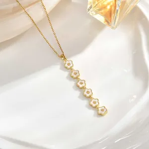 Detail of long gold chain necklace featuring cascading white enamel flowers on ceramic tray