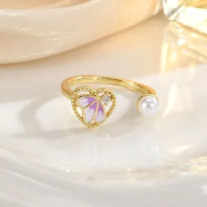 Detail of golden heart ring with purple butterfly wing, white pearl and sparkling diamond
