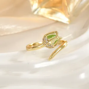 Close-up of golden tulip ring with green gemstone and pavé diamonds on wavy backdrop