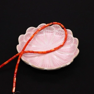 Dettaglio di perline cilindriche arancione-rosse levigate in un piatto di ceramica