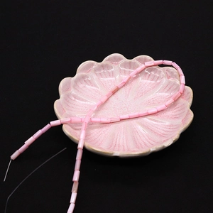 Primo piano di perline cilindriche in conchiglia rosa con trama naturale su piatto a fiori