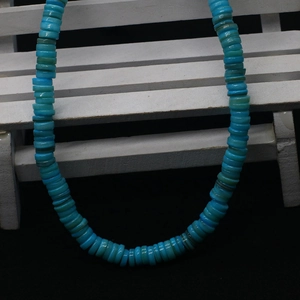 Macro shot of sky blue flat disc freshwater shell beads on a white wooden display stand