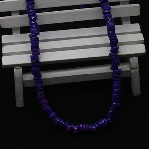 Detailed macro view of purple disc-shaped dyed shell beads hanging on a white wooden stand