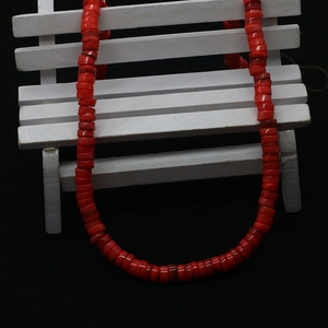 Macro shot of 6-8mm dyed red natural shell flat beads on a mini white wooden bench