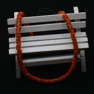 Macro detail of vibrant orange Heishi shell beads strand on a white mini bench