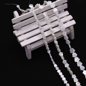 Natürliche weiße Muschelperlen in Blumenform für DIY-Schmuck auf Holz mit schwarzem Grund