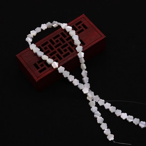 Makroaufnahme von 10 mm weißen Perlmutten-Blumenperlen für Schmuck auf einem Holzsockel