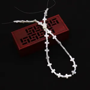 Détail des perles en nacre blanche en forme de croix pour bijoux DIY sur boîte sombre