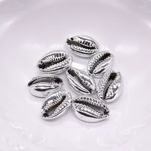 Close-up of eight silver-plated cowrie shell charms on a white plate for DIY jewelry making