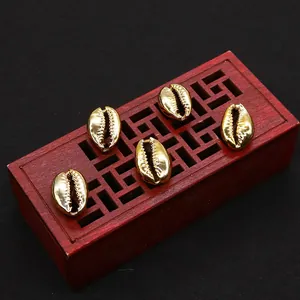 Five gold plated natural conch shell beads for DIY jewelry making on a red wood tray