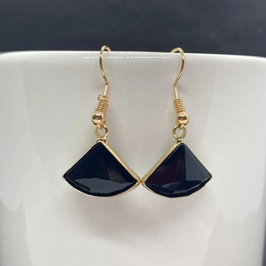 Detail view of fan-shaped black crystal earrings hanging on a white porcelain cup