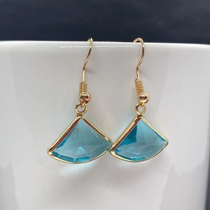Detailed close-up of fan-shaped golden earrings with faceted turquoise stone on porcelain